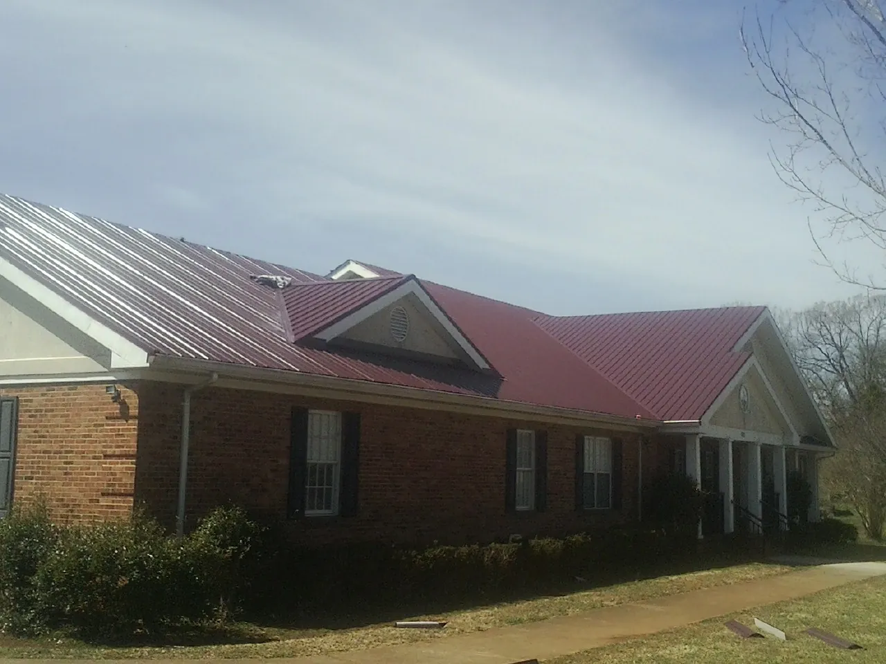 Red metal roof with gabled entries on a long brick building, from a Hail Damage Roof Repair job in Linkwood