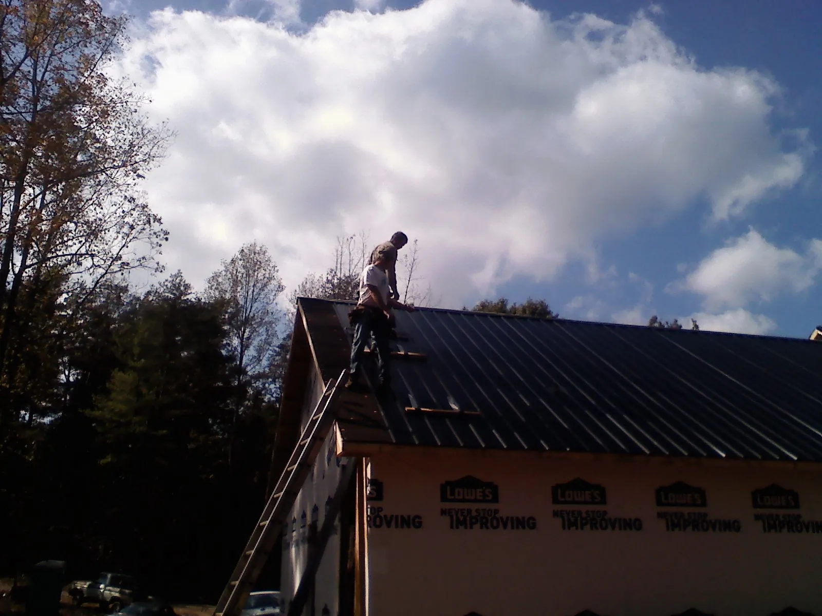Roofer fastening dark metal panels high against a cloudy sky, from a Roof Inspection job in Linkwood