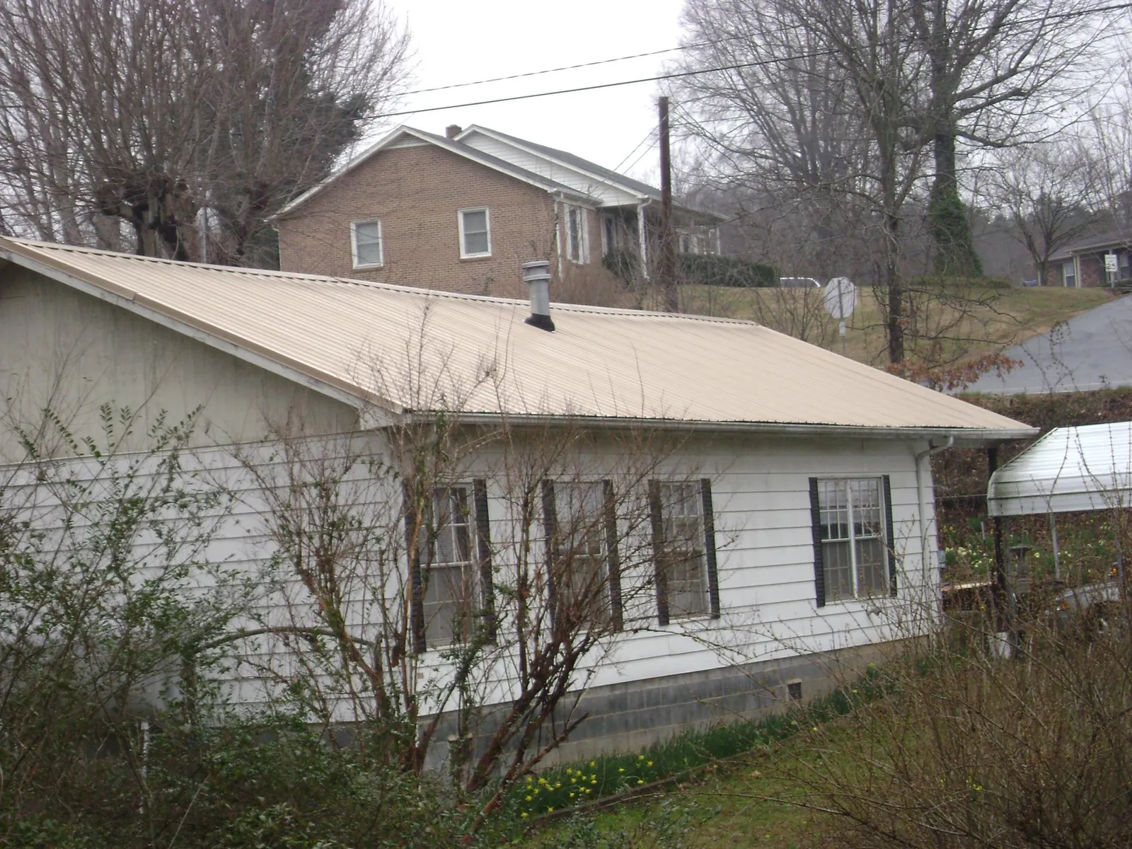 Tan metal roof on a white sided house set into a hillside — Commercial Roofing by Roofing Brothers in Linkwood