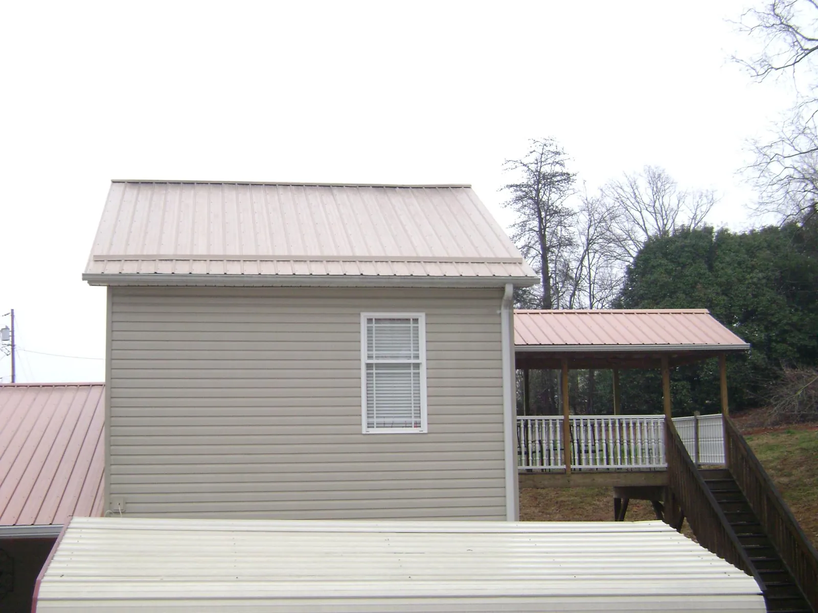 Tan metal roofs on a two story addition and attached porch, from a Roof Replacement job in Linkwood